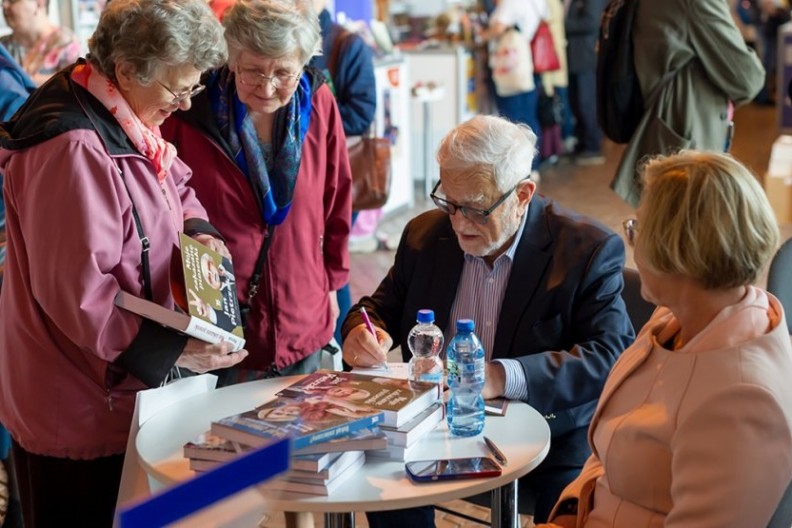 Jan Pietrzak podpisuje książkę „Moje zakazane piosenki” podczas XXIX Tragów Wydawców Katolickich. W prawym rogu widoczna Barbara Nowak. Fot. Michał Klag/Biały Kruk