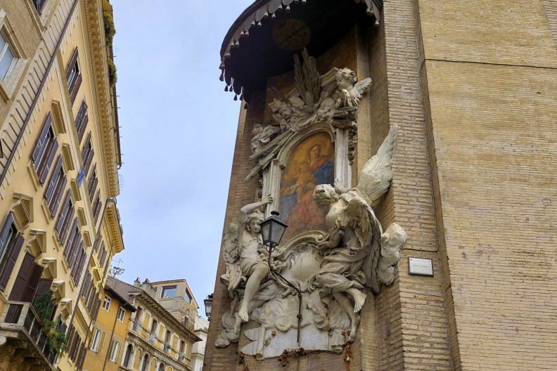 Zdjęcie przedstawia rzymską „Madonnellę” – bogato zdobioną kapliczkę z wizerunkiem Maryi, umieszczoną na rogu ulicy, na ścianie budynku. Kapliczka jest otoczona barokową oprawą z rzeźbami aniołów i ozdobnym baldachimem. Fot. Turismo Roma